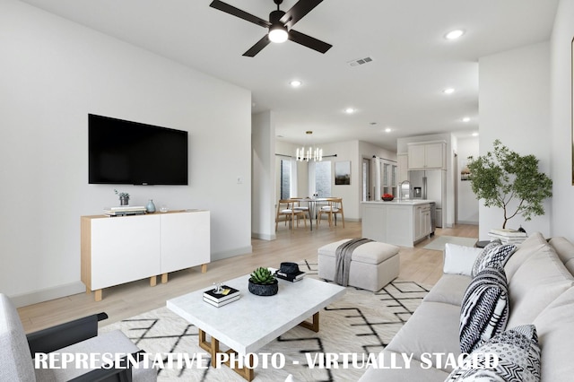 living room with ceiling fan with notable chandelier, sink, and light hardwood / wood-style flooring