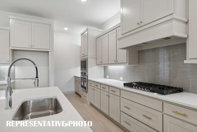 kitchen with light wood-type flooring, backsplash, stainless steel appliances, sink, and white cabinets