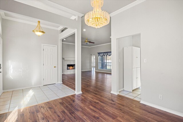 tiled entrance foyer with a tiled fireplace, crown molding, and ceiling fan with notable chandelier