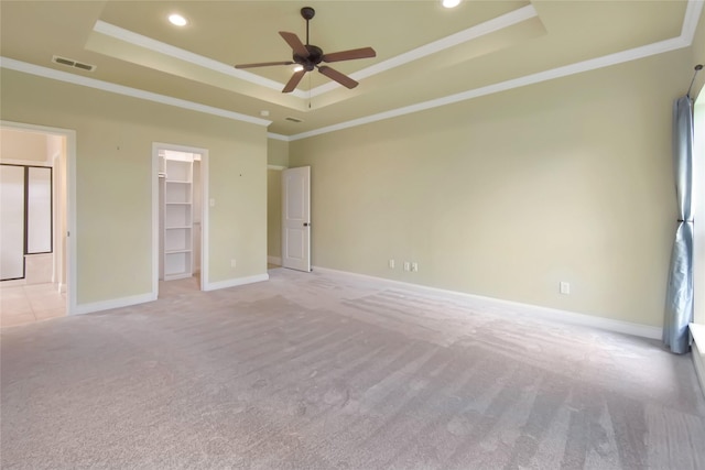 unfurnished bedroom featuring ceiling fan, a walk in closet, crown molding, and a tray ceiling