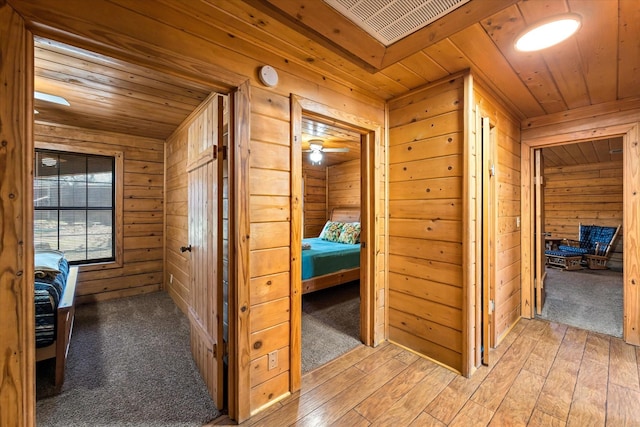 hallway featuring wood walls, wooden ceiling, and light wood-type flooring