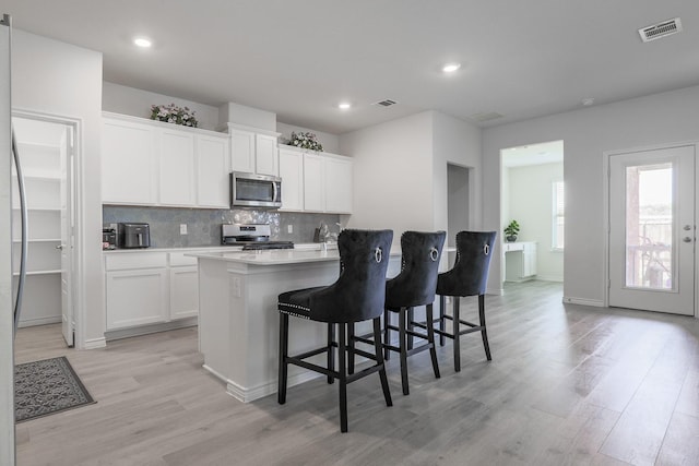 kitchen featuring white cabinets, a kitchen breakfast bar, light hardwood / wood-style floors, and appliances with stainless steel finishes