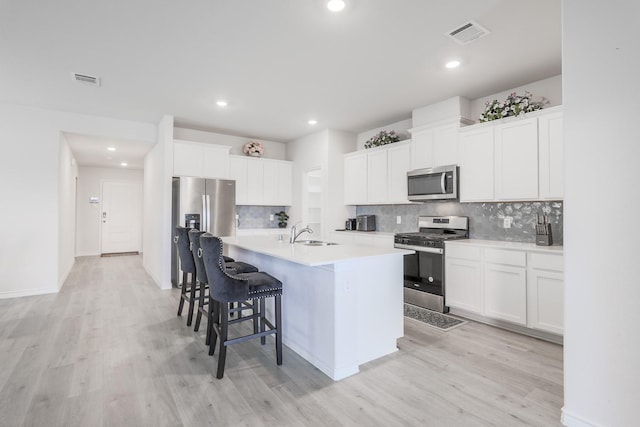 kitchen with stainless steel appliances, white cabinetry, a center island with sink, and light hardwood / wood-style flooring