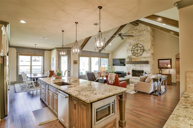 kitchen featuring a stone fireplace, sink, plenty of natural light, light stone counters, and stainless steel appliances