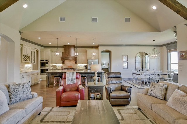 living room featuring an inviting chandelier, ornamental molding, high vaulted ceiling, and light hardwood / wood-style flooring