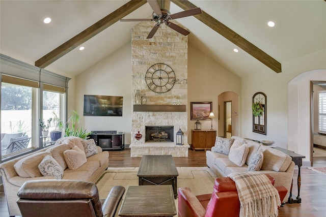 living room with ceiling fan, high vaulted ceiling, beamed ceiling, a fireplace, and light hardwood / wood-style floors