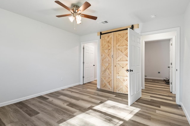 unfurnished bedroom with ceiling fan, a barn door, and light hardwood / wood-style floors