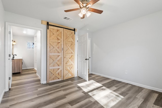 unfurnished bedroom with hardwood / wood-style flooring, a barn door, and ceiling fan