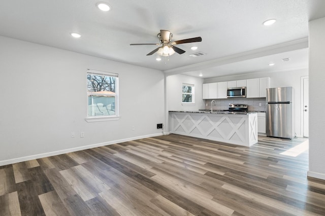 interior space featuring white cabinetry, hardwood / wood-style floors, stainless steel appliances, tasteful backsplash, and kitchen peninsula