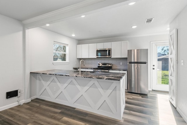 kitchen with appliances with stainless steel finishes, backsplash, white cabinets, dark stone counters, and kitchen peninsula