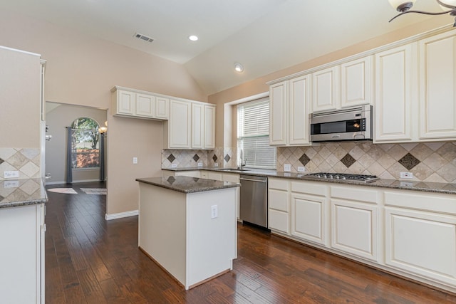 kitchen featuring dark hardwood / wood-style flooring, stainless steel appliances, a kitchen island, and dark stone counters