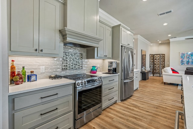 kitchen with crown molding, gray cabinetry, backsplash, stainless steel appliances, and light wood-type flooring