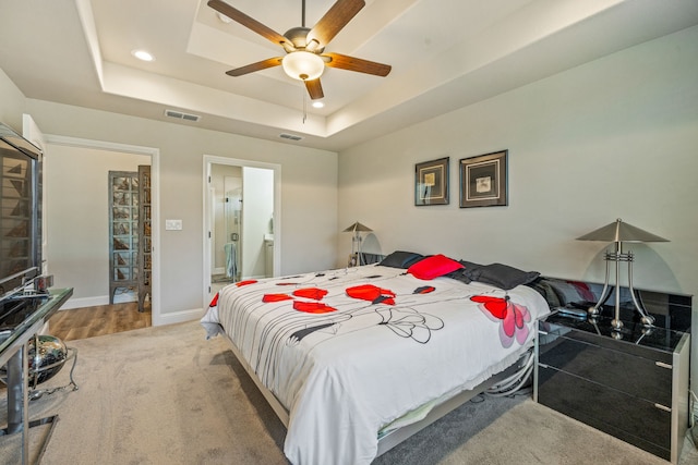 carpeted bedroom featuring ceiling fan, a tray ceiling, and ensuite bath