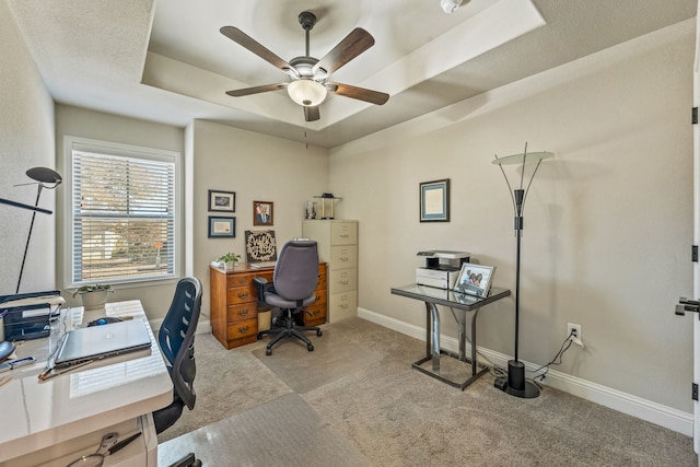 carpeted home office with ceiling fan and a raised ceiling