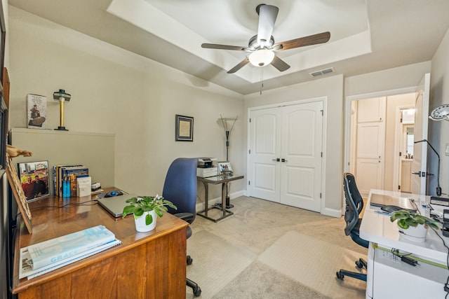 home office featuring light carpet, a tray ceiling, and ceiling fan