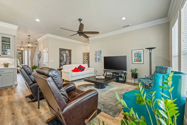 living room featuring ceiling fan with notable chandelier, ornamental molding, and light wood-type flooring