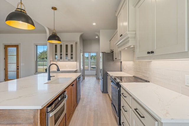 kitchen featuring hanging light fixtures, an island with sink, white cabinets, and light stone counters