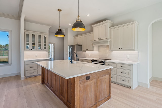 kitchen with decorative light fixtures, a kitchen island with sink, light stone counters, stainless steel appliances, and light hardwood / wood-style flooring