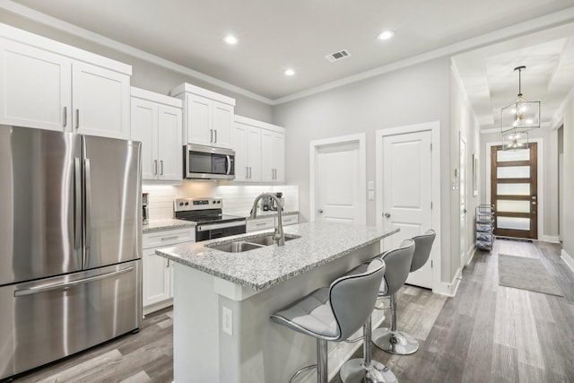 kitchen with sink, stainless steel appliances, light stone counters, a center island with sink, and white cabinets