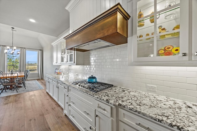 kitchen featuring stainless steel gas stovetop, decorative backsplash, light wood-type flooring, custom range hood, and white cabinetry