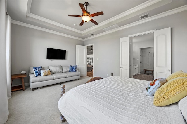 carpeted bedroom with a tray ceiling, ensuite bath, ceiling fan, and ornamental molding