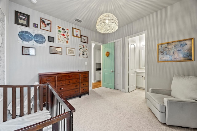 carpeted bedroom featuring a nursery area, an inviting chandelier, and ensuite bath