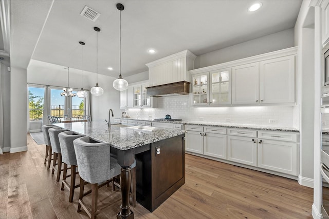 kitchen featuring white cabinets, stainless steel gas stovetop, a center island with sink, and light hardwood / wood-style flooring