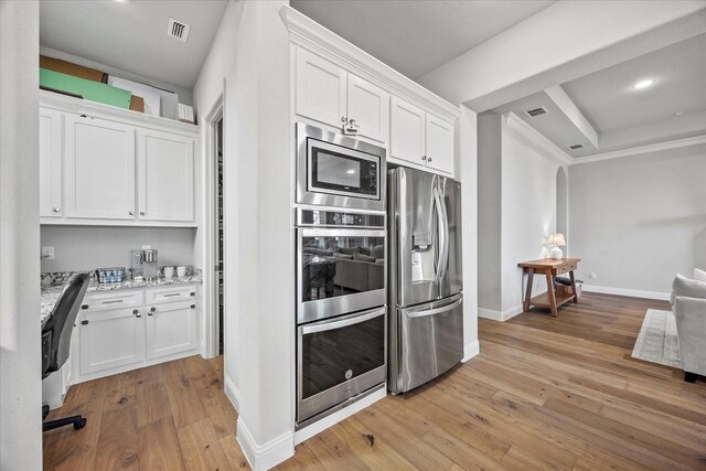 kitchen with light stone counters, white cabinets, stainless steel appliances, and light wood-type flooring