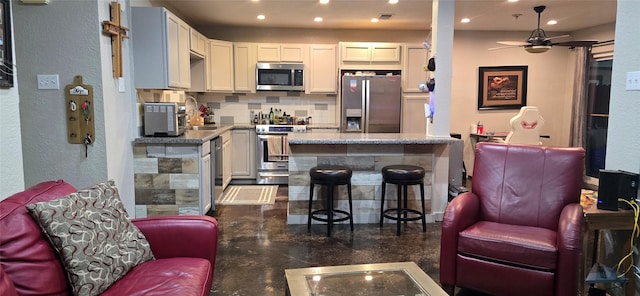 kitchen featuring a kitchen bar, backsplash, stainless steel appliances, ceiling fan, and white cabinets