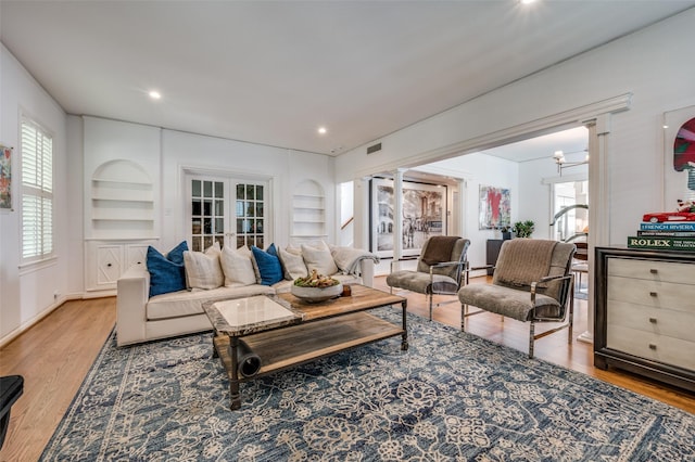 living room featuring hardwood / wood-style floors, built in shelves, an inviting chandelier, and french doors