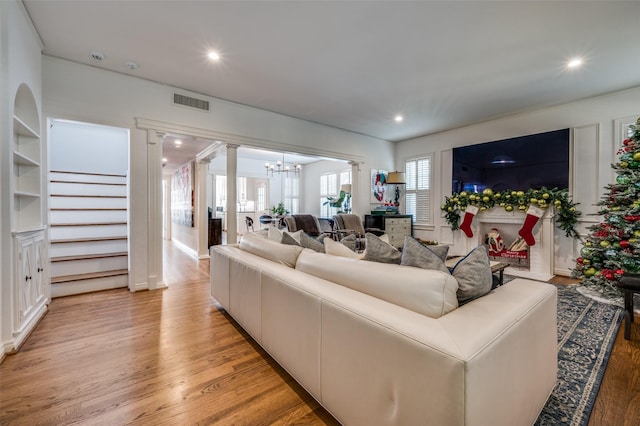 living room with light hardwood / wood-style floors, decorative columns, and a notable chandelier