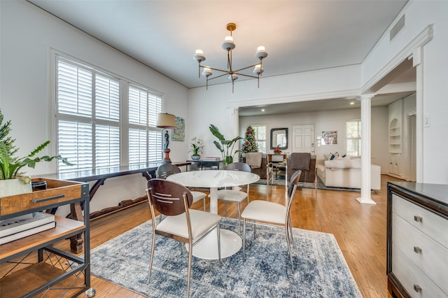 dining area with an inviting chandelier, light hardwood / wood-style flooring, and ornate columns