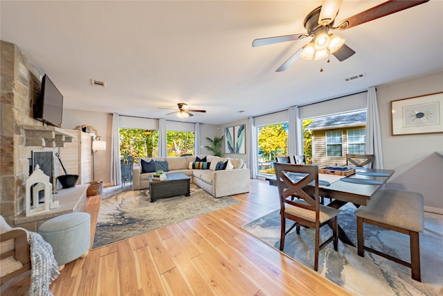 living room featuring a stone fireplace, light hardwood / wood-style floors, and ceiling fan