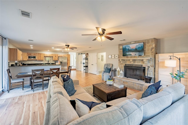 living room featuring a stone fireplace, light hardwood / wood-style flooring, and ceiling fan