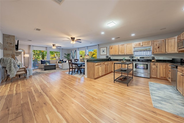 kitchen with appliances with stainless steel finishes, light brown cabinetry, a breakfast bar, ceiling fan, and light hardwood / wood-style flooring