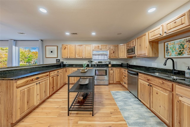 kitchen featuring appliances with stainless steel finishes, dark stone counters, sink, light brown cabinets, and light hardwood / wood-style floors