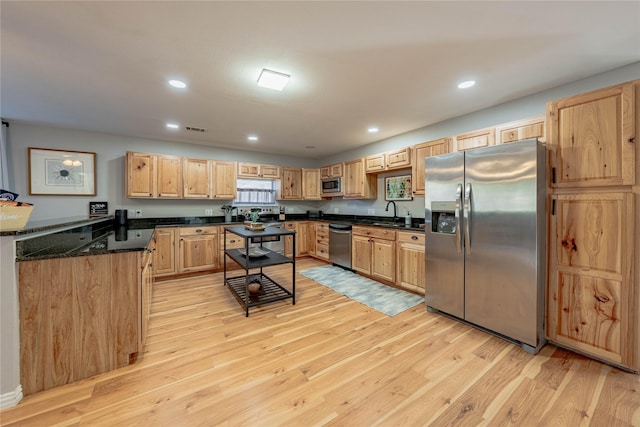 kitchen featuring appliances with stainless steel finishes, light wood-type flooring, light brown cabinets, and dark stone countertops