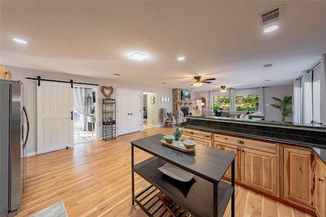 kitchen featuring ceiling fan, stainless steel fridge, a barn door, light wood-type flooring, and a fireplace