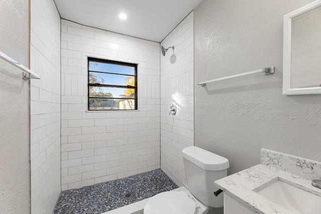 bathroom with tiled shower, vanity, and toilet