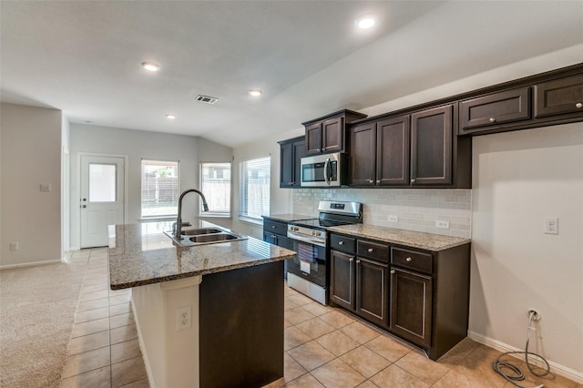 kitchen with stainless steel appliances, vaulted ceiling, a kitchen island with sink, sink, and light tile patterned floors