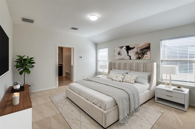 carpeted bedroom with ensuite bath and lofted ceiling