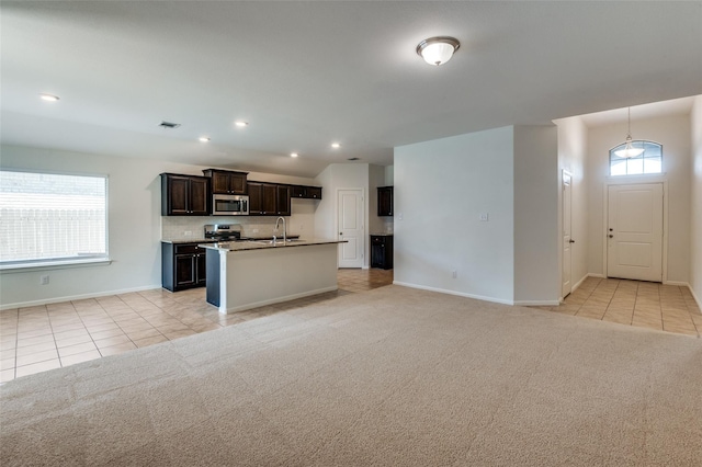 kitchen featuring sink, light colored carpet, decorative backsplash, a center island with sink, and appliances with stainless steel finishes