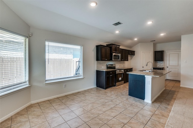 kitchen featuring sink, vaulted ceiling, light stone countertops, an island with sink, and stainless steel appliances