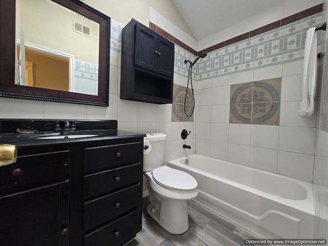 full bathroom featuring lofted ceiling, tiled shower / bath, hardwood / wood-style flooring, toilet, and tile walls