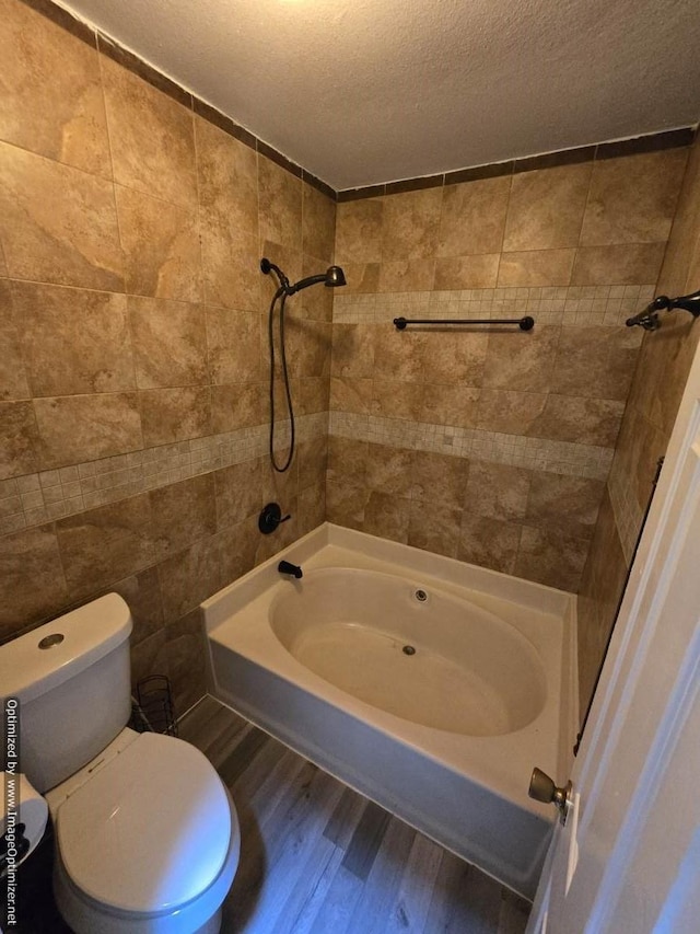 bathroom featuring hardwood / wood-style floors, tiled shower / bath, toilet, tile walls, and a textured ceiling