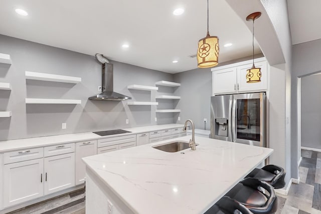 kitchen featuring sink, stainless steel refrigerator with ice dispenser, hanging light fixtures, wall chimney exhaust hood, and white cabinetry