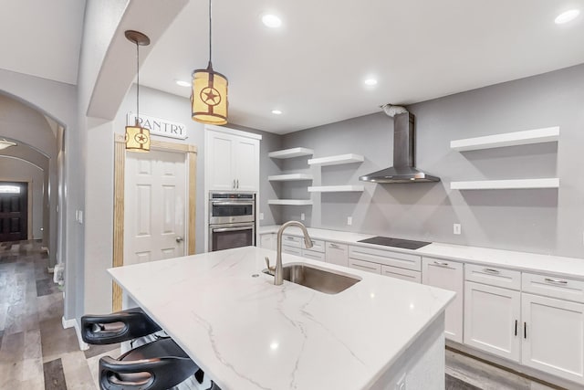 kitchen featuring wall chimney range hood, sink, decorative light fixtures, light hardwood / wood-style flooring, and white cabinetry