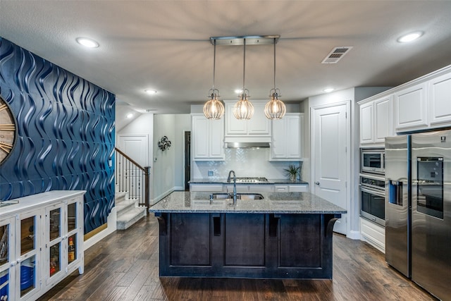 kitchen with dark wood-type flooring, stone countertops, a sink, backsplash, and stainless steel appliances