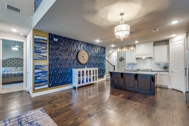 kitchen with a breakfast bar area, visible vents, dark wood-type flooring, white cabinets, and under cabinet range hood