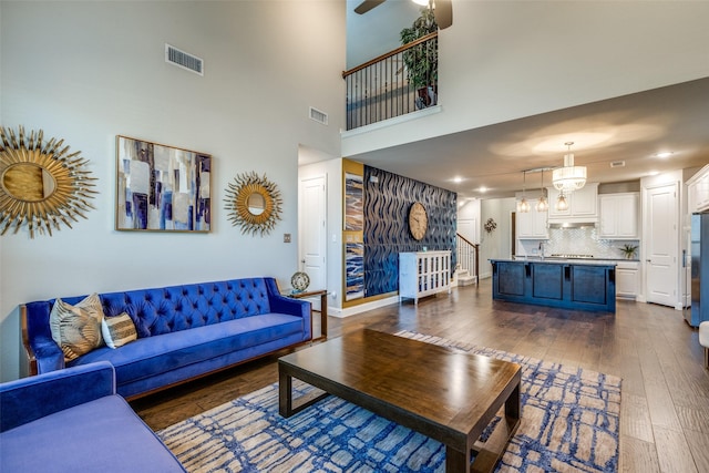 living room with dark wood-type flooring, ceiling fan with notable chandelier, visible vents, and baseboards